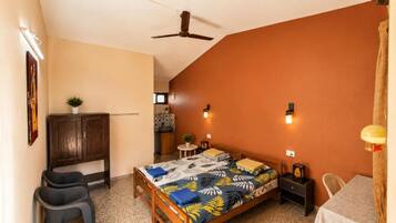 A bedroom with a bed, two bedside tables, a nightstand, a desk, a chair, a ceiling fan, and a wall-mounted light fixture.