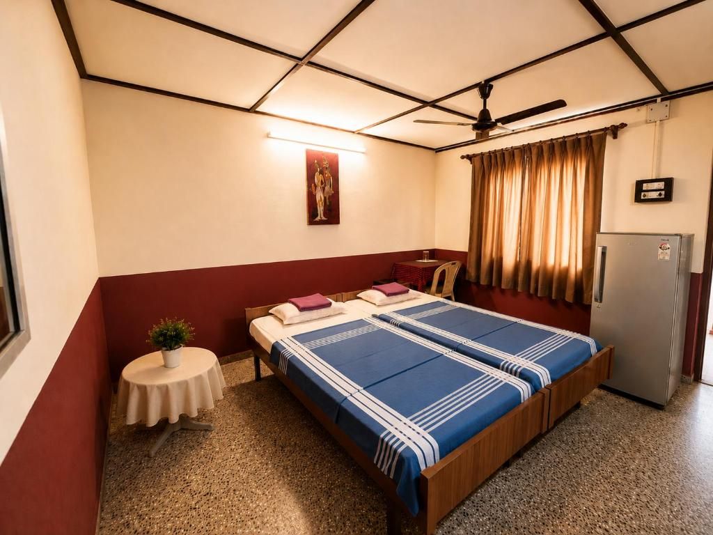 A single-bed room with a wooden bed, a small table with a plant, a ceiling fan, and a refrigerator.
