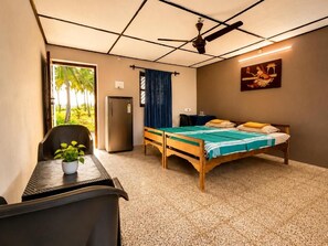 Una habitación con cama, escritorio, silla, planta en maceta, ventilador de techo y ventana con vista a palmeras.