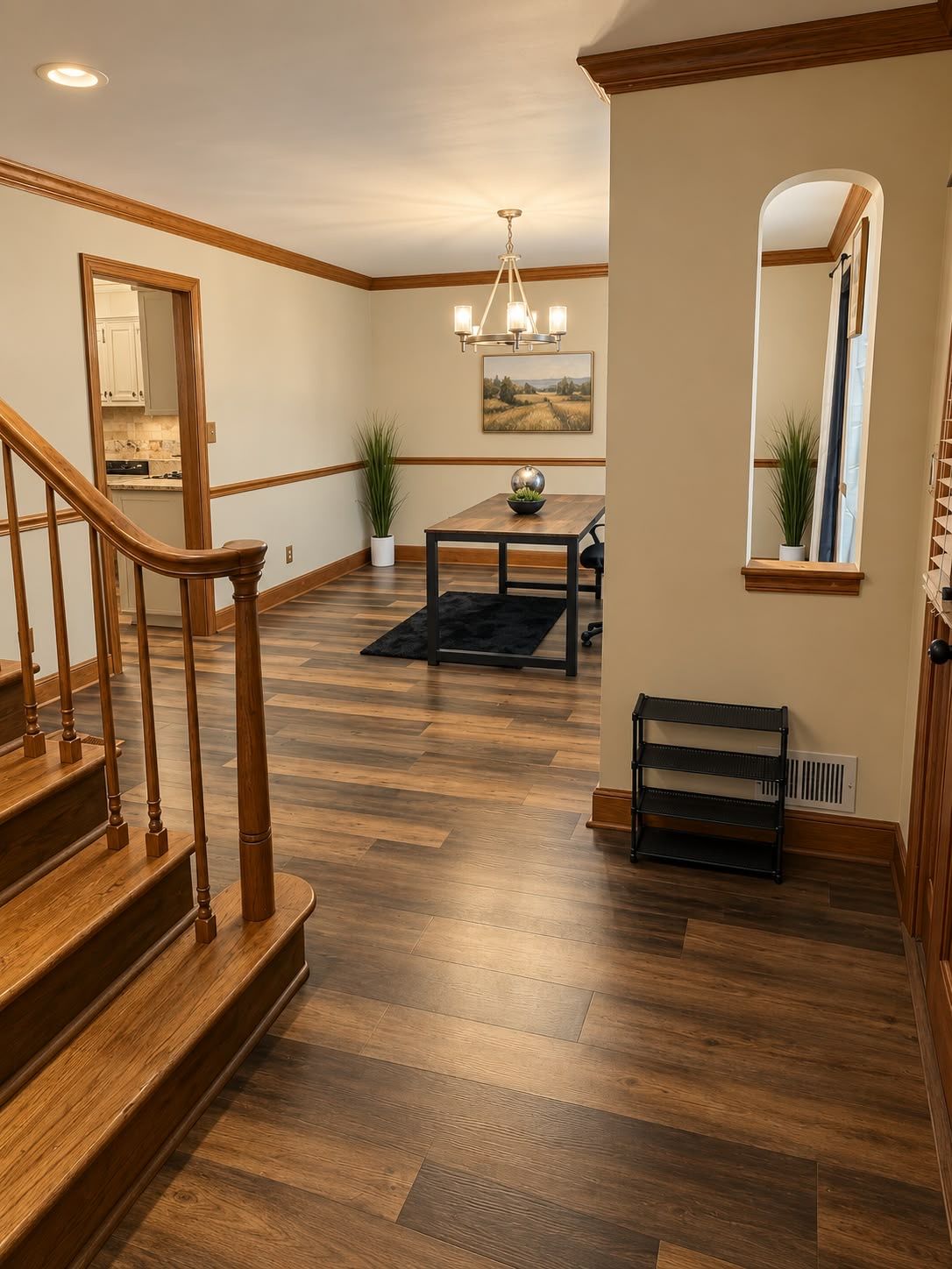 A spacious room with a wooden staircase, a dining area with a chandelier, and a view of the kitchen.
