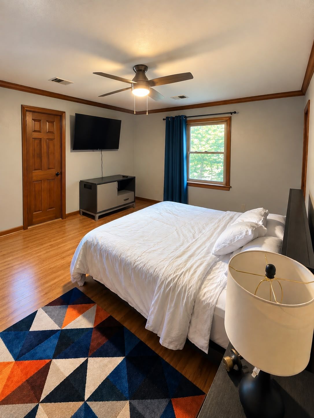 A bedroom with a bed, a television, a ceiling fan, and a window with curtains.