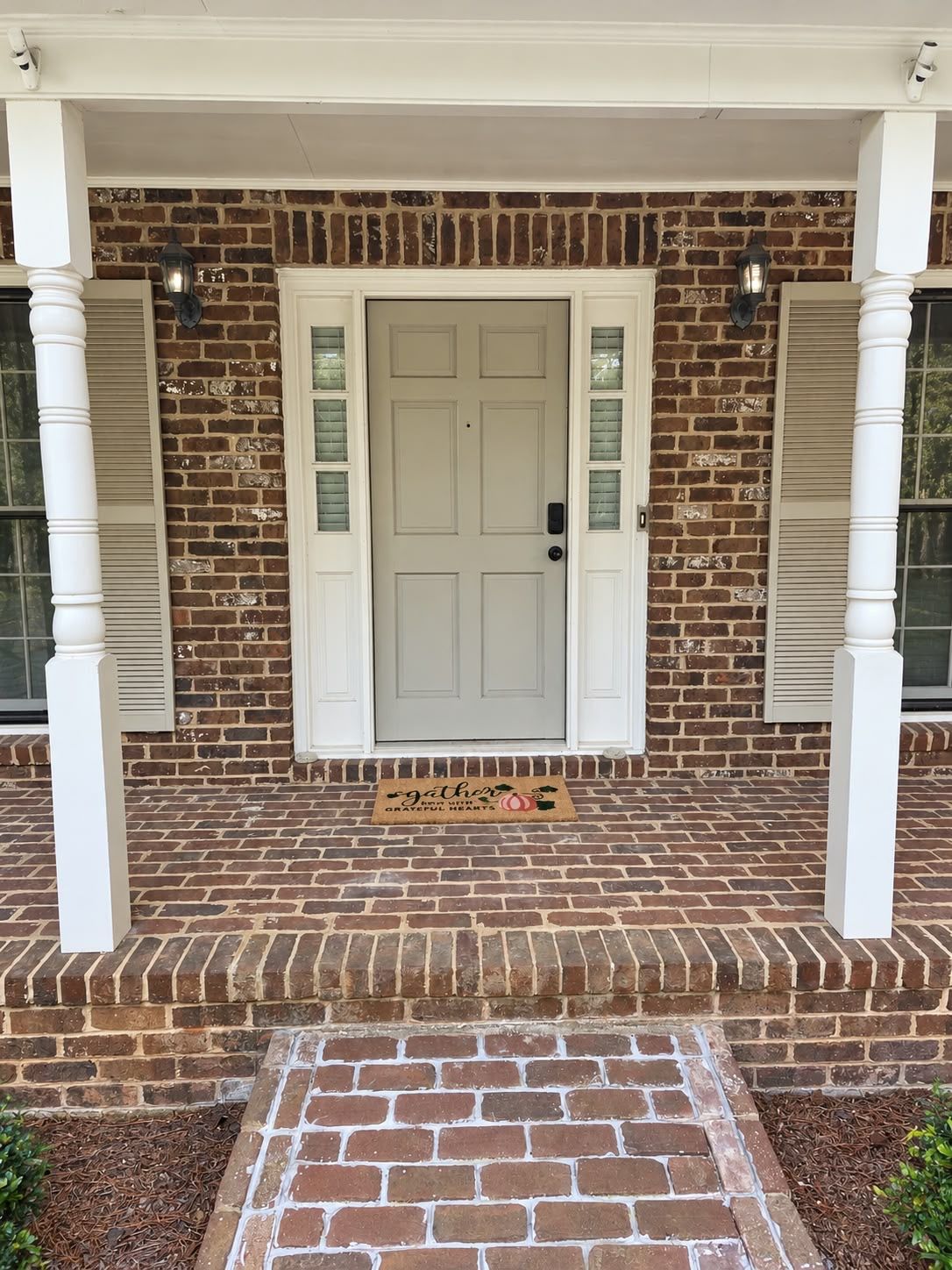 A brick house with a white front door, a doormat, and a small porch area.