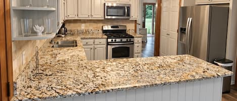 A kitchen with white cabinetry, a granite countertop, stainless steel appliances, and a hanging light fixture.