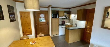 A compact kitchen with a dining table, wooden cabinets, and a microwave.