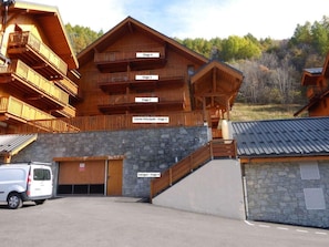 A multi-story wooden building with balconies, a stone facade, and a parking area. - 50m from ski slopes, 3rd floor, swimming pool, sauna, ski locker, 40m², Valloire (Valloire)