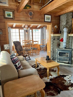 A cozy log cabin interior with a sofa, chairs, a fireplace, and a dining area.