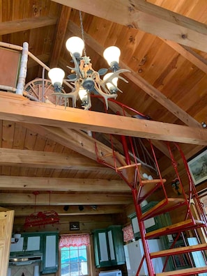 A wooden interior with a chandelier, red metal staircase, and a window with curtains.