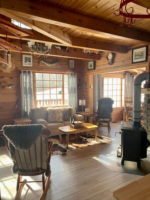 A cozy cabin interior with a sofa, chairs, a table, a fireplace, and wooden walls.