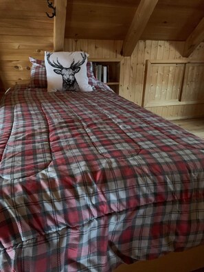 Un letto con copriletto a quadri in una stanza di una baita di legno.