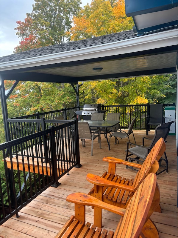 A covered outdoor deck with a grill, wooden chairs, and a table.