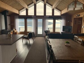A cabin interior with a dining area, kitchen, and large windows overlooking a lake.