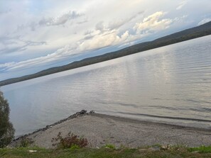 A calm lake with a rocky shoreline and a forested hill in the background. - Maison du Lac (Témiscouata-sur-le-Lac)