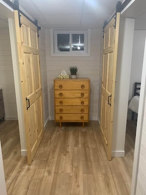 A narrow hallway with wooden flooring, a central wooden dresser with drawers, and two sliding doors on either side.
