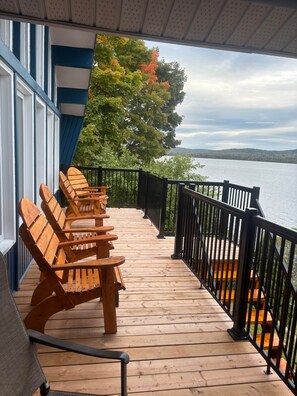 A wooden deck with Adirondack chairs, a railing, and a view of a lake.