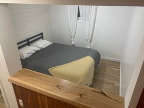 A bedroom with a bed, a wooden bench, and a window with curtains. - Maison du Lac (Témiscouata-sur-le-Lac)
