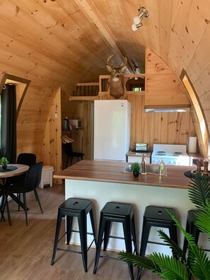A wooden interior with a kitchen area, a dining table with chairs, and a bar stool area.