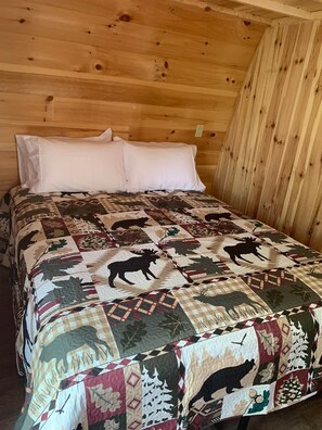 A wooden cabin room with a bed covered in a patterned quilt. - Le chalet de la rivière (Saint-Eusèbe)