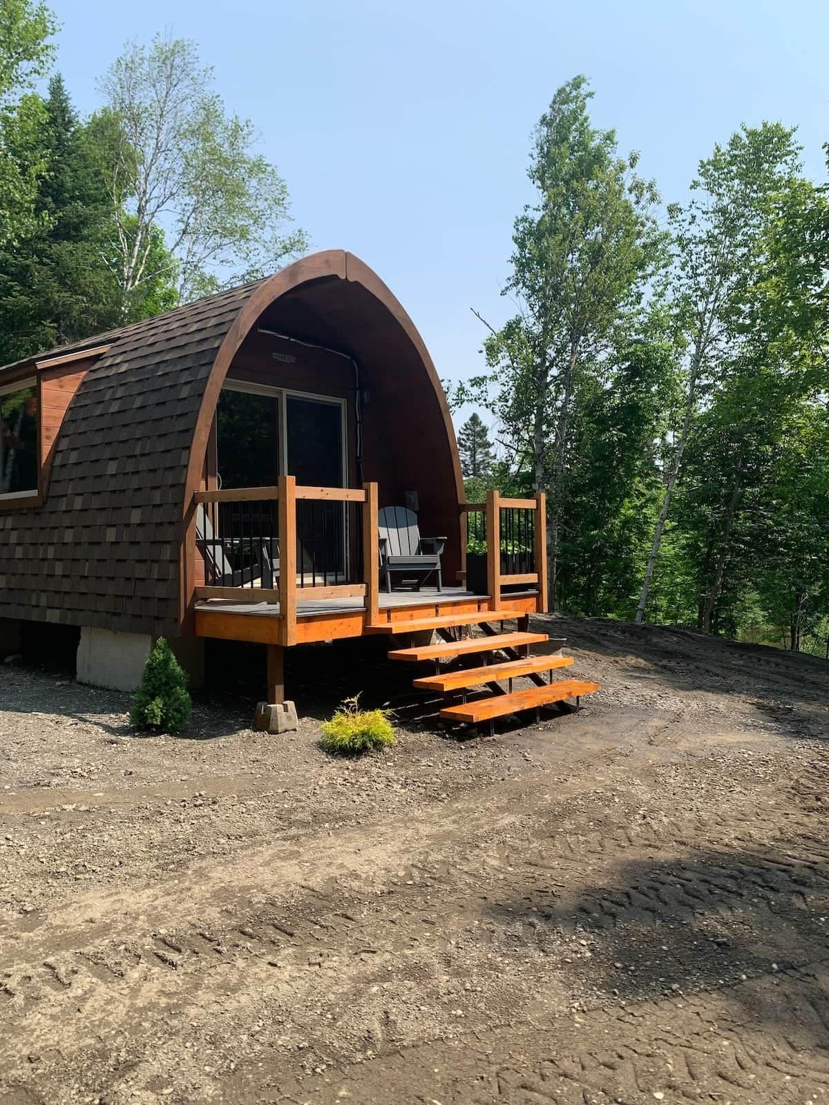 A single-story, semi-circular wooden cabin with a porch and a small deck.