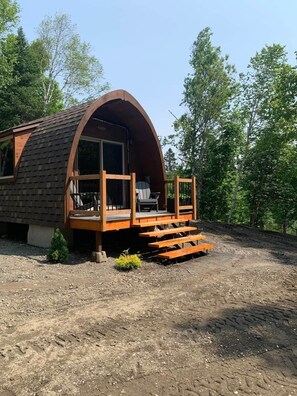 A single-story, semi-circular wooden cabin with a porch and a small deck. - Le chalet de la rivière (Saint-Eusèbe)