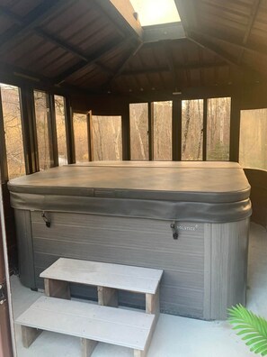 A hot tub with a bench and a table in a covered outdoor area. - Le chalet de la rivière (Saint-Eusèbe)