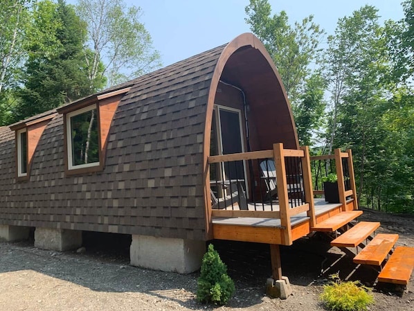 A small cabin with a sloped roof, a porch with benches, and a door leading to a covered area.