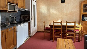 A compact kitchen with wooden cabinets, a microwave, a sink, and a dining area with a table and chairs. - 350m from ski slopes, 1st floor, balcony, tv, ski locker, 30m², Valloire (Valloire)