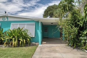 Une maison de plain-pied à la façade de couleur turquoise, dotée d’un porche et d’un jardin devant, où l’on trouve des plantes tropicales.