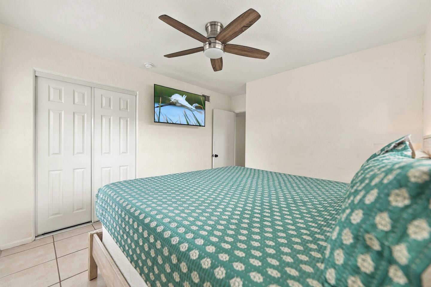 Une chambre à coucher avec un lit, un ventilateur de plafond, une télévision et une porte.