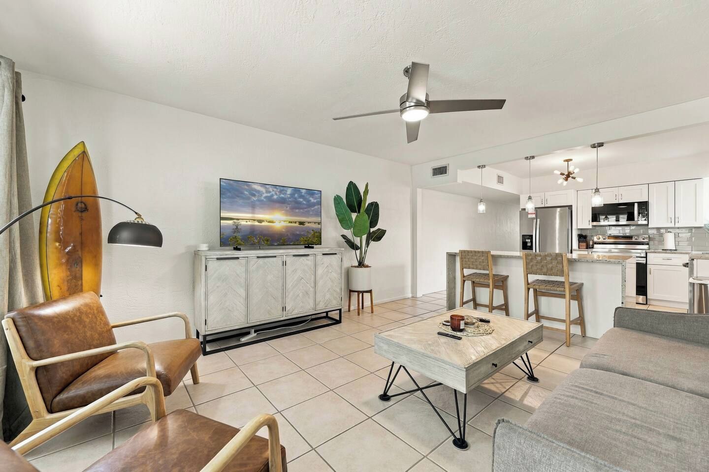 A modern living room with a sofa, chairs, a coffee table, a TV, and a ceiling fan.