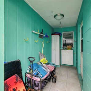 Un couloir étroit aux murs de couleur turquoise, une porte blanche et une petite fenêtre avec des stores. Un chariot contenant des sacs et un balai se trouve au premier plan.