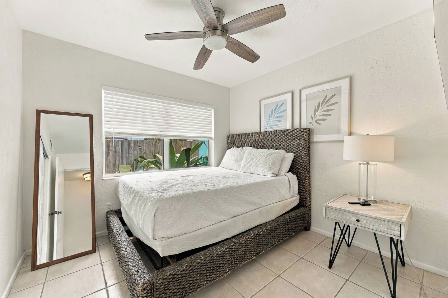A bedroom with a bed, a ceiling fan, a bedside table with a lamp, and a window with blinds.