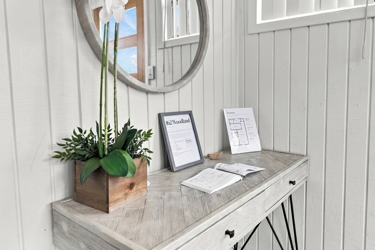 A wooden console table with a framed sign, a potted plant, and a mirror.