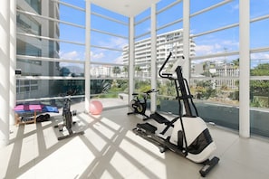 Een ruime fitnessruimte met diverse trainingsapparaten, grote ramen en uitzicht op een woongebied.