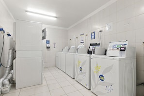 Een schone, moderne wasserette met meerdere wasmachines en drogers, een ventilatiesysteem en informatieposters aan de muur.