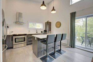 A modern kitchen with stainless steel appliances, a central island with bar stools, and a large window with a view.