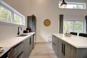 A modern kitchen with a central island, a built-in sink, and a clock on the wall. - La Catherine  - Weedon (Weedon)