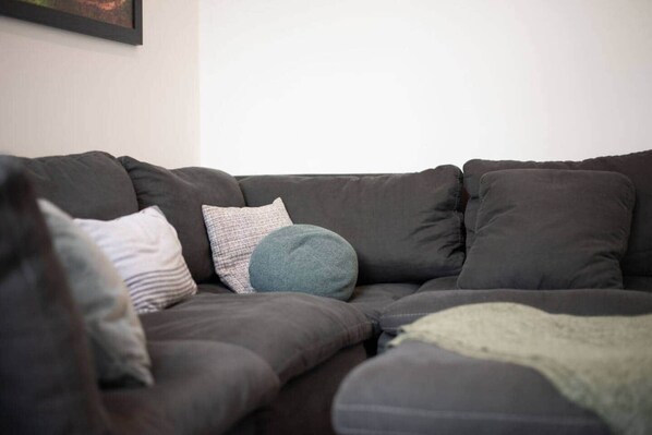 A dark-colored sofa with multiple cushions in a room with plain walls.