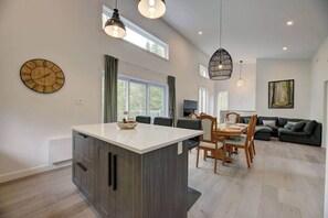 A modern kitchen with a central island, dining area with chairs, and a living room with a sofa. - La Catherine  - Weedon (Weedon)