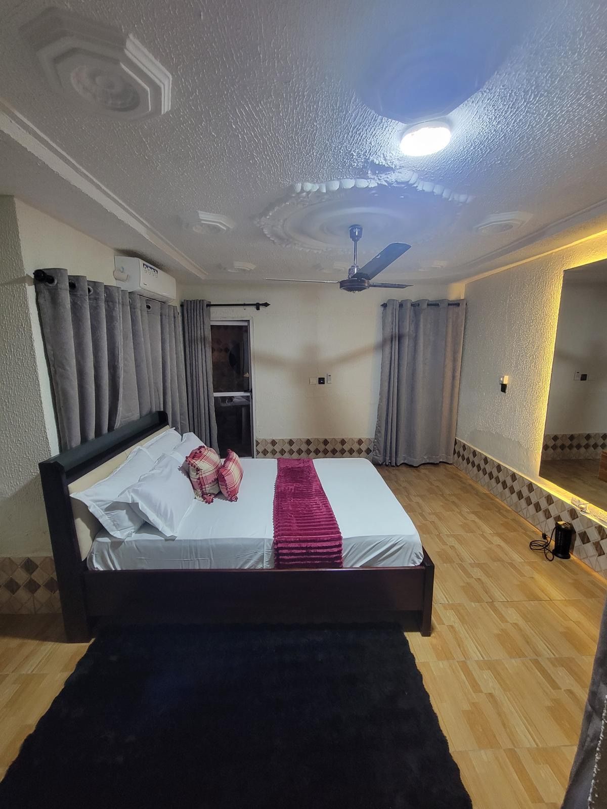 Una camera d'albergo con un letto, tende, una ventola a soffitto e uno specchio.