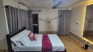 Una camera d'albergo con un letto, tende, una ventola a soffitto e uno specchio.