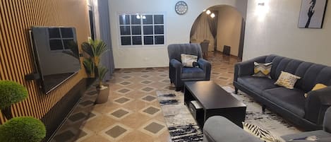 A living room with a sofa, armchairs, a coffee table, a TV, and a patterned rug.