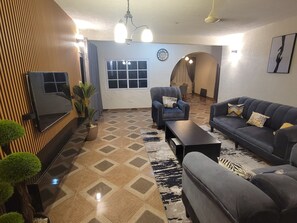 Una sala de estar con un sofá, sillones, una mesa de centro, un televisor y un tapete estampado.
