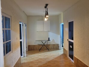 Un pasillo con suelo de madera, una mesa con un planchado y una lámpara en el techo.
