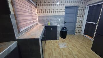 A compact kitchen with a tiled backsplash, a wooden countertop, a black trash bin, and a door.