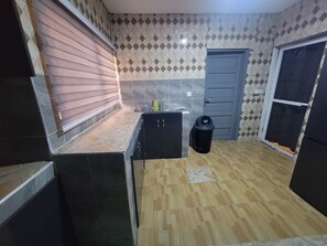 A compact kitchen with a tiled backsplash, a wooden countertop, a black trash bin, and a door.