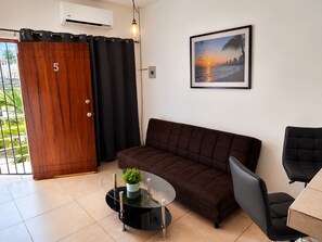 A modern living room with a brown sofa, a glass coffee table with a plant, a black armchair, and a framed picture of a sunset on the wall. - Cozy apartment Independencia condo with AC in vibrant Puerto Vallarta (Puerto Vallarta)
