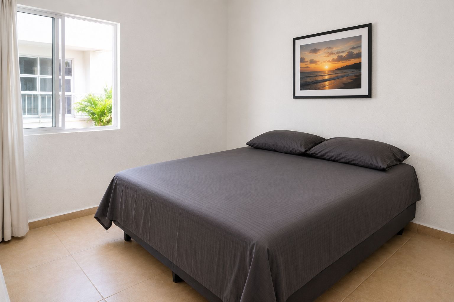 Una cama bien hecha con una colcha oscura y almohadas en una habitación con un ventanal grande y un cuadro en la pared.