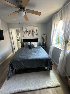 A bedroom with a bed, a ceiling fan, a window with curtains, and artwork on the wall.