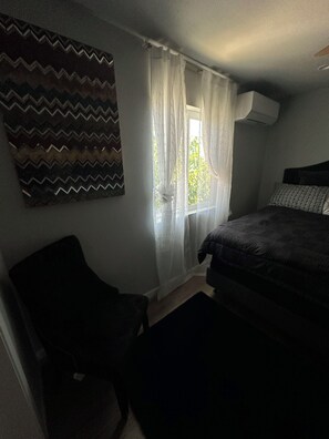 A bedroom with a bed, a chair, a window with curtains, and a wall with a zigzag pattern.