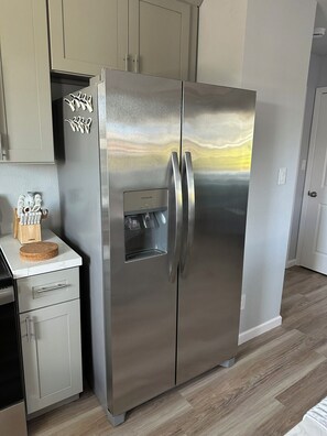 A stainless steel refrigerator with a water dispenser, a wooden utensil holder, and a cork coaster on a white countertop.